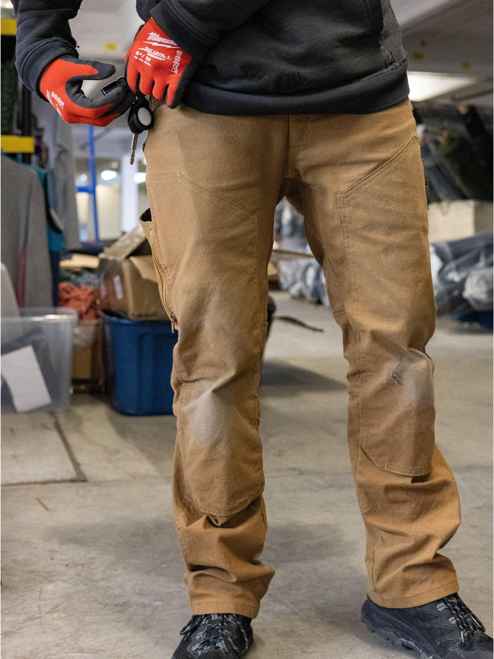 A tradesman in a workshop wearing tan American-made double knee work pants by 1620 USA, highlighting the reinforced front knee panels designed for heavy-duty wear.