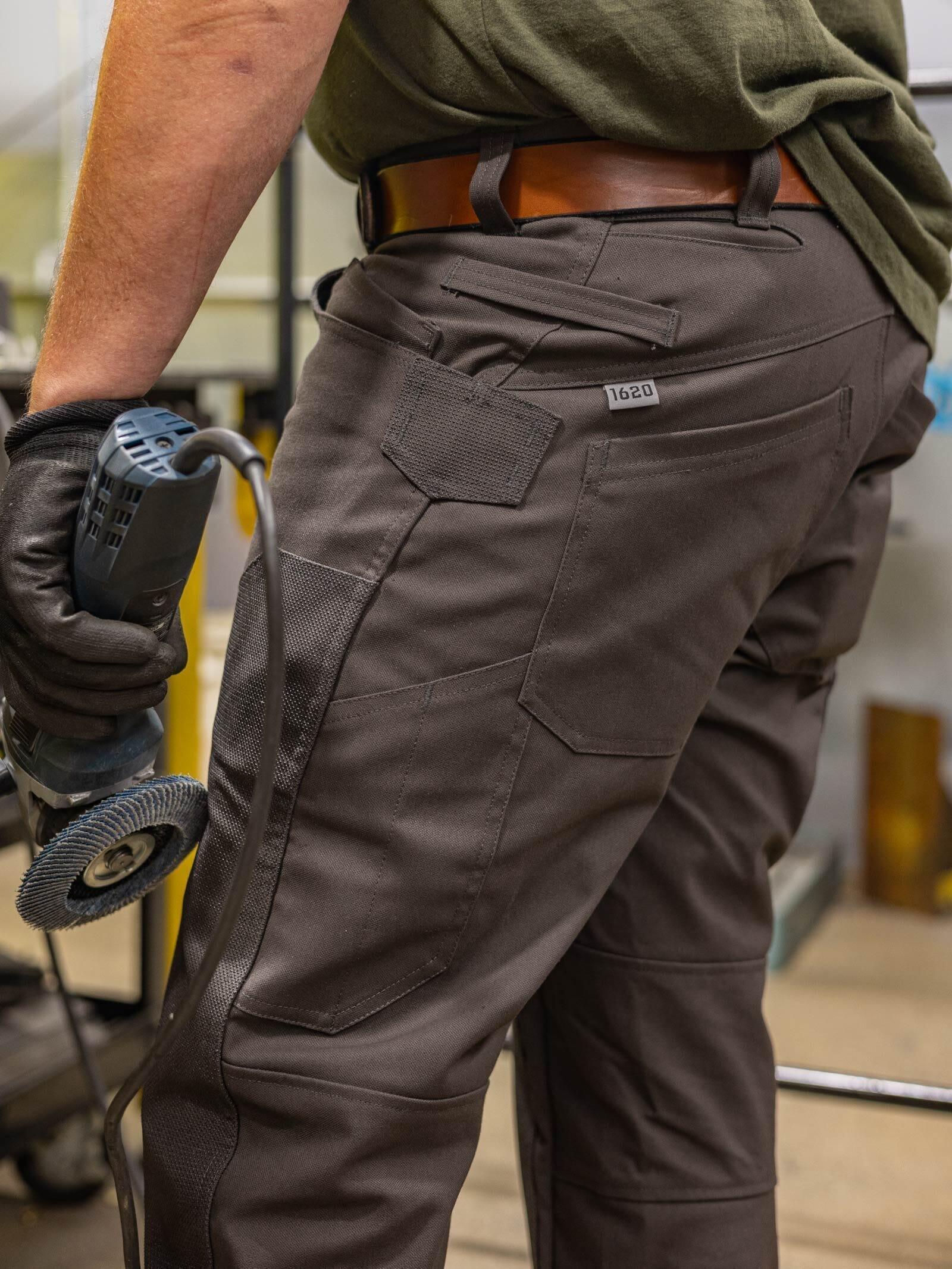 A tradesman holding a power grinder wearing dark grey 1620 USA men's work pants, showcasing reinforced utility pockets and a modern articulated fit.